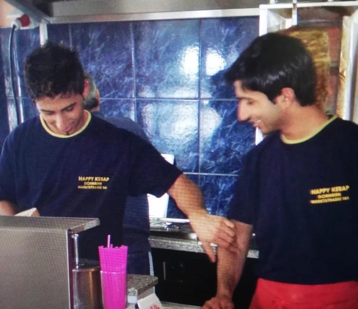 Zwei junge Männer in „Happy Kebap Dornbirn“-Shirts lachen hinter der Theke